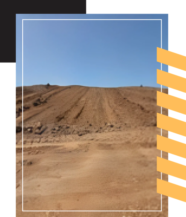 A wide view of a brown dirt field and sloped embankment under a clear sky.