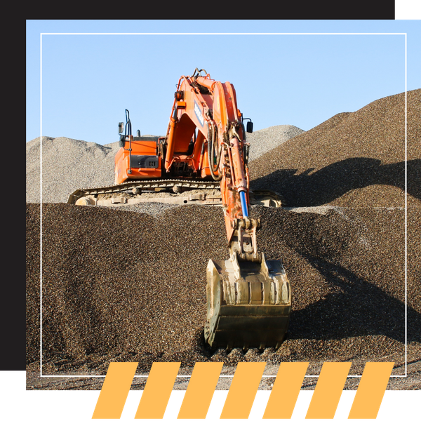 An orange excavator digging into a large mound of dark gravel.