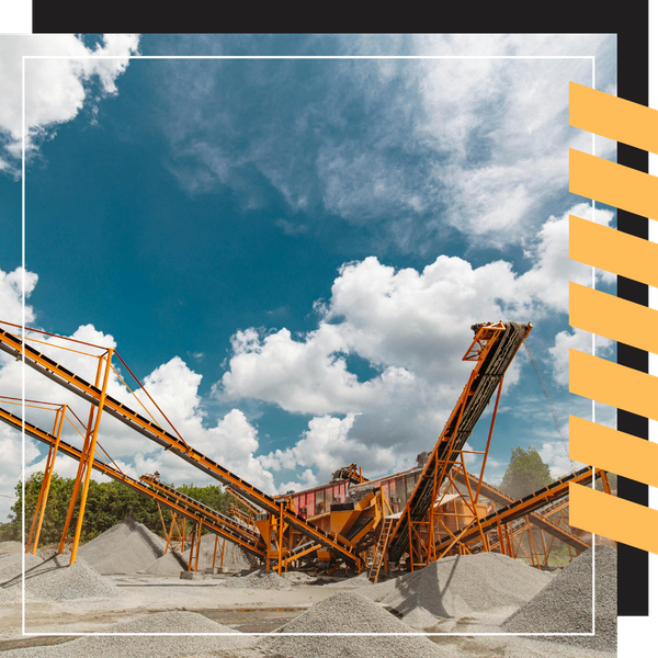 Multiple orange industrial conveyor belts extending over piles of gravel.