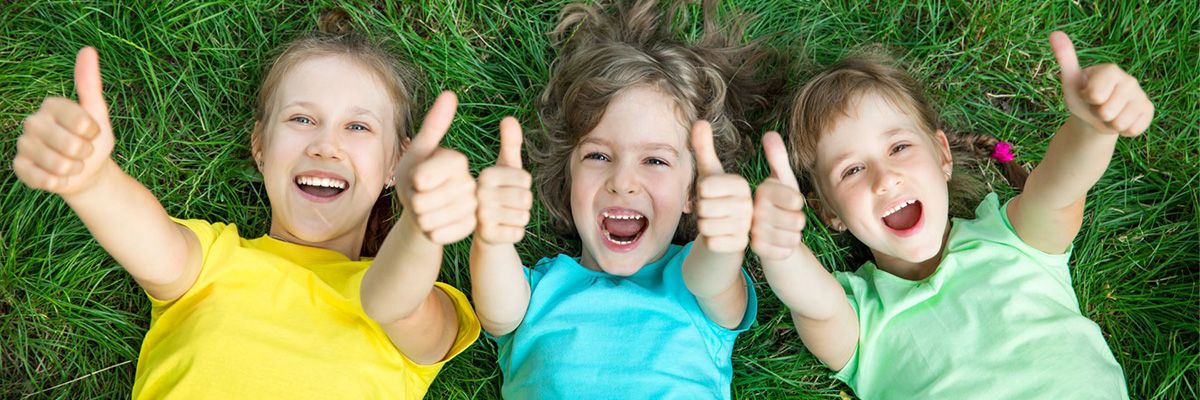 3 children lying on grass giving thumbs uip