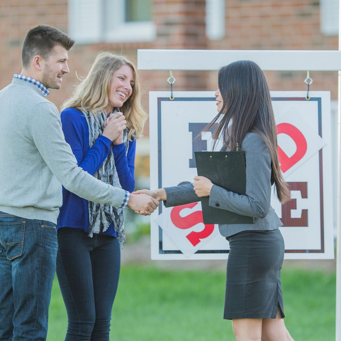 Real estate agent shaking hands with couple in front of sold sign