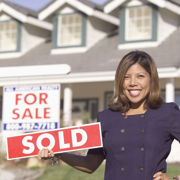 Real estate agent smiling and holding "SOLD" sign in front of house