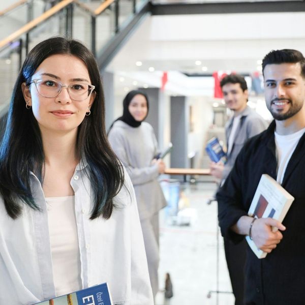 A diverse group of professional individuals stands together in a modern, multi-level office building atrium.