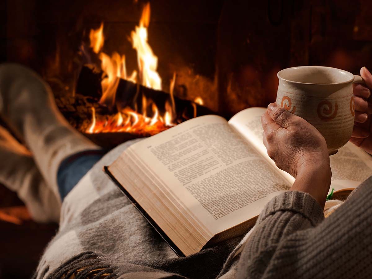 Person reading by the fire under a blanket