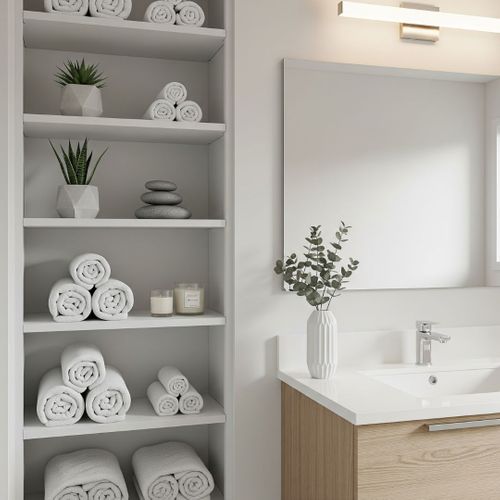 A set of clean, white, built-in shelves next to a bathroom vanity, neatly organized with rolled towels and decor.