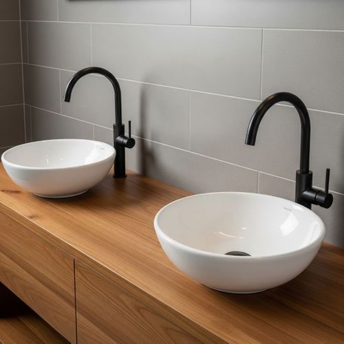 A close-up of a modern wooden double vanity with two white vessel sinks and sleek black faucets against a tiled wall.
