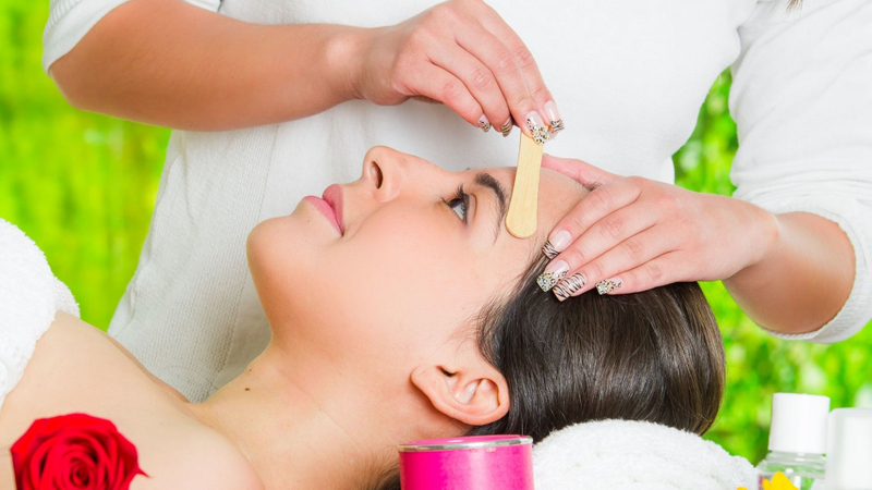 Stylist applies wax to a woman's forehead with a wooden stick. Stylist applies wax to a woman's forehead with a wooden stick.