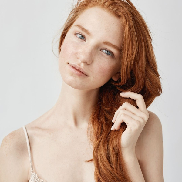 Redhead woman gently touching her long, vibrant hair.