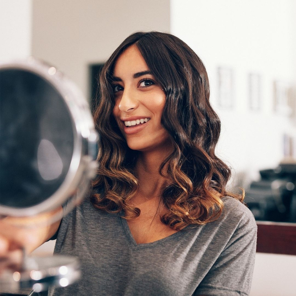 Woman checking wavy, styled hair in a handheld mirror.