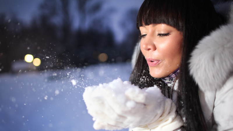 Woman in winter gear gently blows snow from her gloved hands. Woman in winter gear gently blows snow from her gloved hands.