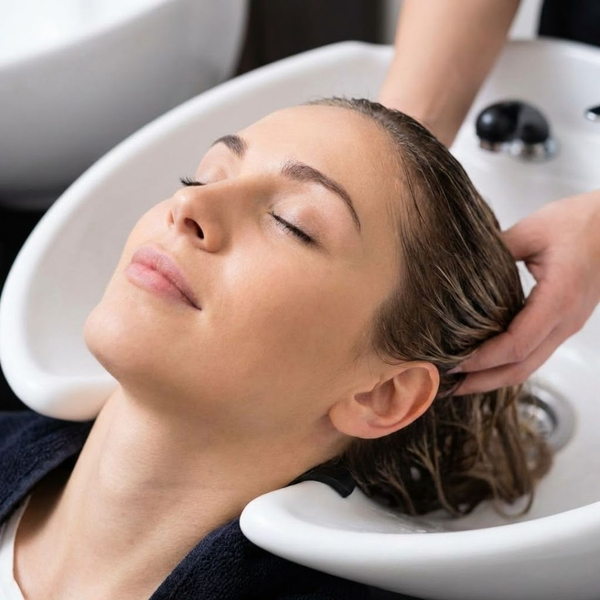 A client with a relaxed expression and closed eyes receives a head massage at a salon shampoo bowl