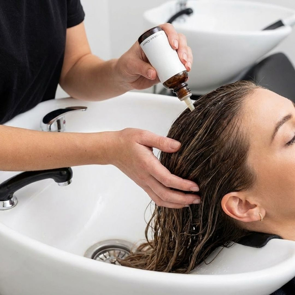 a therapist applying a scalp treatment product to a client's hair at a salon shampoo bowl