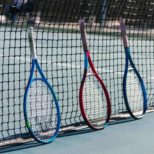 3 Tennis racquets leaning on tennis court net