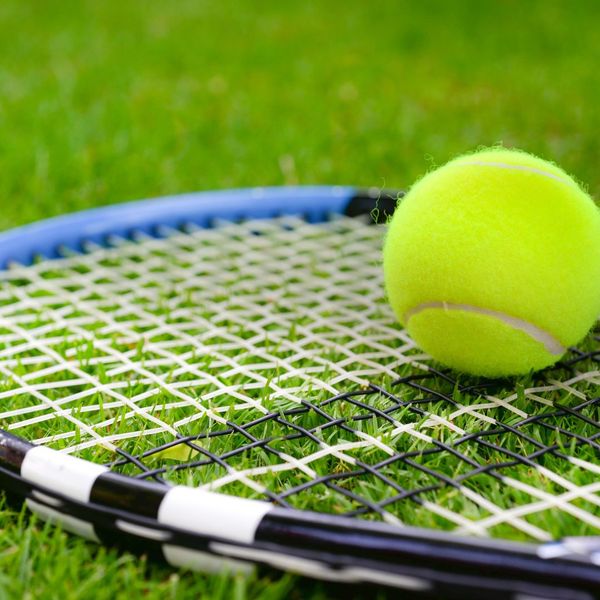 tennis ball on top of tennis racquet on grass