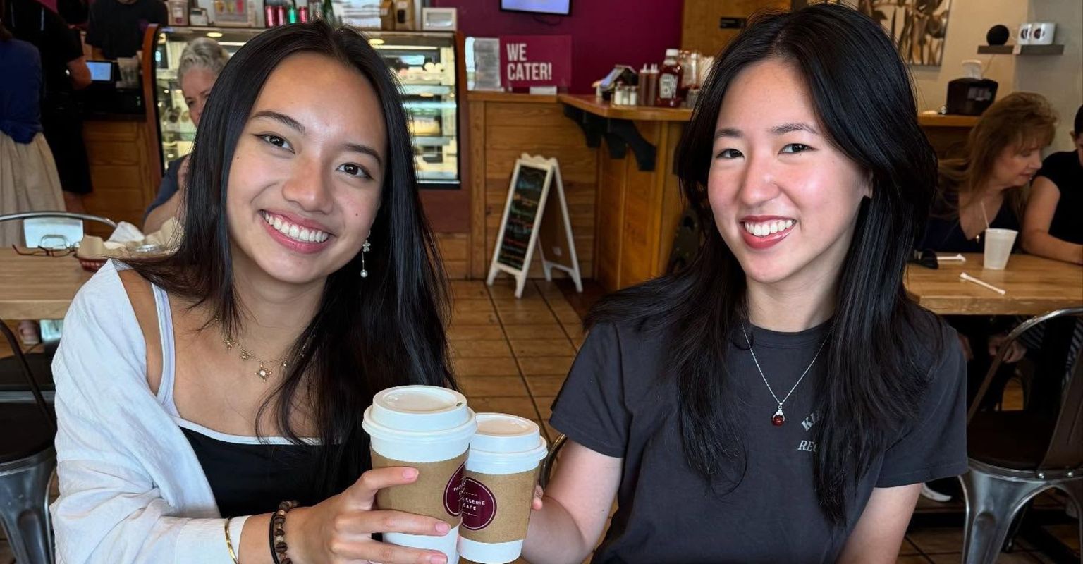 Two friends laughing together at a sunlit cafe table.
