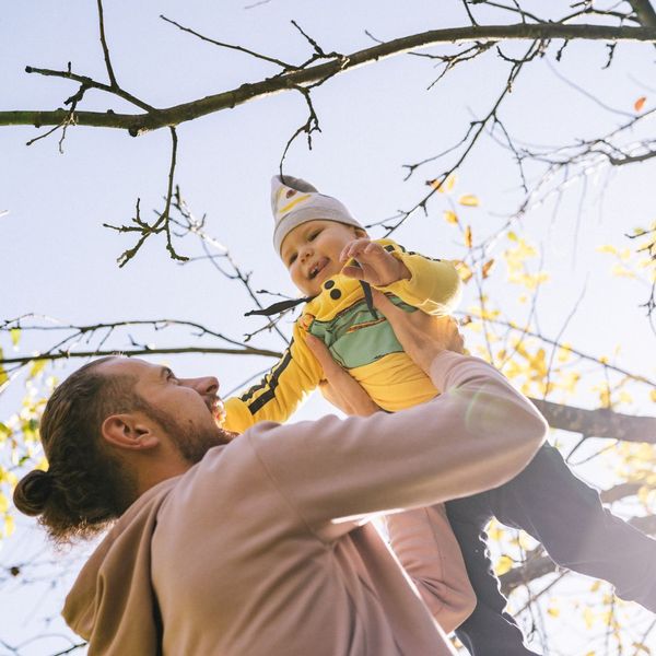 Man lifting up a baby with a tree in the background