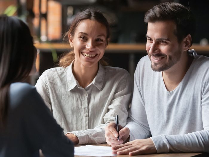 Image of a young couple signing a contract during a meeting with an insurance agent.