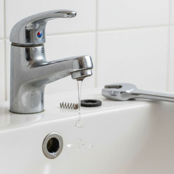 Image showing a close-up of a slow, steady drip from a modern kitchen faucet, illustrating a common household leak caused by worn internal components. Image showing a close-up of a slow, steady drip from a modern kitchen faucet, illustrating a common household leak caused by worn internal components.