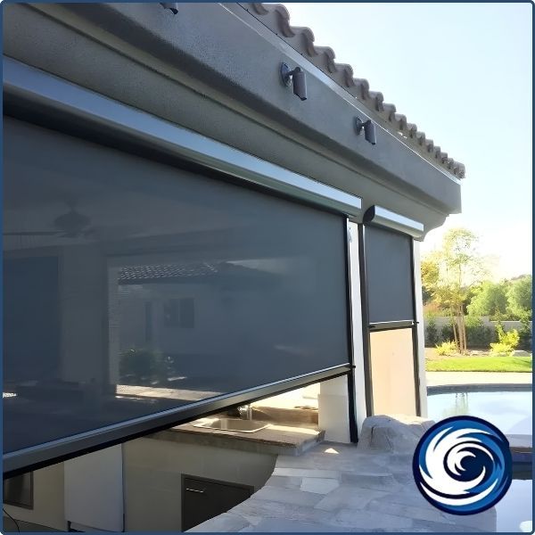 A high-end outdoor kitchen and pool area featuring a black motorized retractable screen being lowered to provide shade and insect protection.