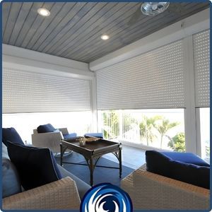 Interior view of a balcony protected by white motorized roll-down hurricane shutters with small perforations to allow light while maintaining storm security.