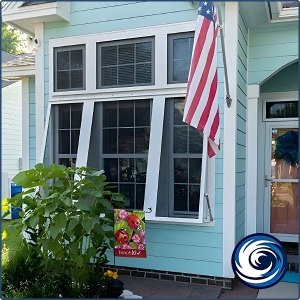 A light blue house with a white-trimmed window display featuring functional Bahama shutters and an American flag.