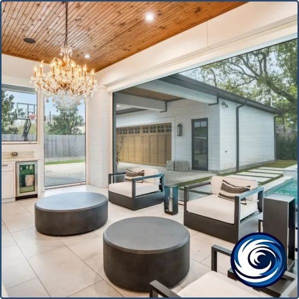 High-end indoor-outdoor transition room with wood-plank ceilings, a crystal chandelier, and large open apertures protected by recessed motorized screens.
