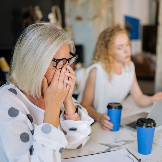 A middle-aged woman looking frustrated or tired while sitting at a table—representing symptoms like fatigue, brain fog, or hormonal stress.