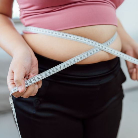Close-up of a person measuring their waist with a measuring tape, representing medical weight loss and metabolic health tracking.