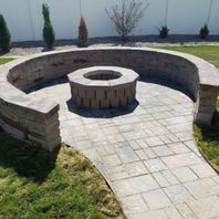 A high-angle shot of a custom-built circular stone fire pit area with integrated curved stone seating benches on a paved patio.