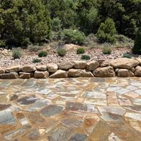 Professional landscaping featuring a tiered natural stone retaining wall and a flagstone patio walkway surrounded by drought-tolerant plants.