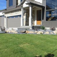 Modern residential home exterior featuring a manicured green lawn, a contemporary gray garage door, and a decorative rock garden border.