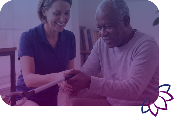 A healthcare professional assists an elderly man as he practices using an adaptive reacher tool to grab an object.