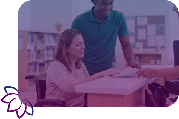 A caregiver assists a woman in a wheelchair as they review paperwork together at a community service counter.