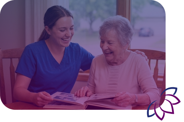 caregiver and an elderly woman share a laugh while looking at a photo album together