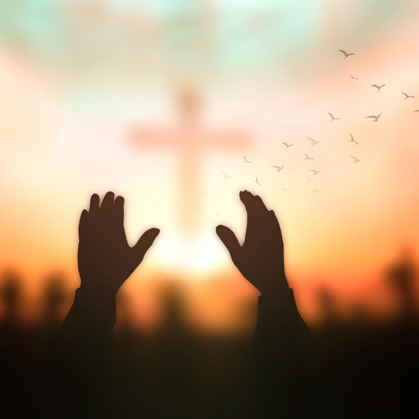 Person raising their hands up with a large, illuminated cross in front of them. 
