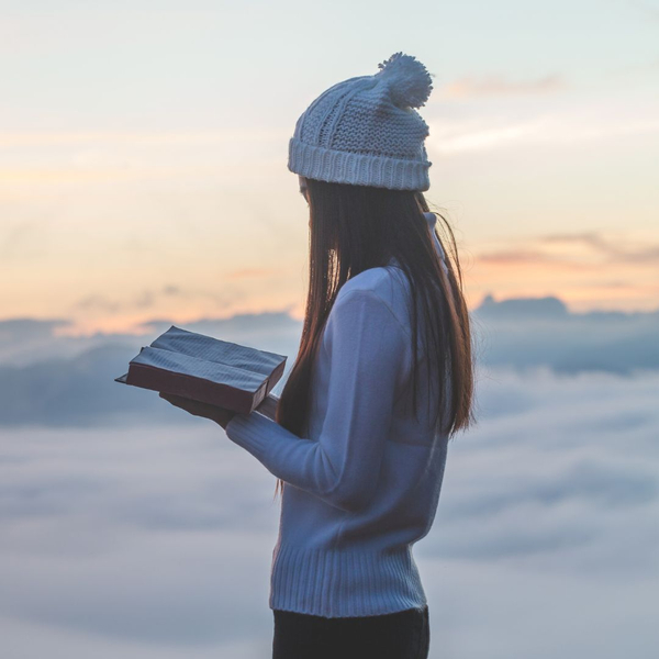 Young woman above the clouds reading a Bible. 
