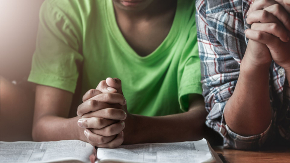 Two kids praying over a Bible