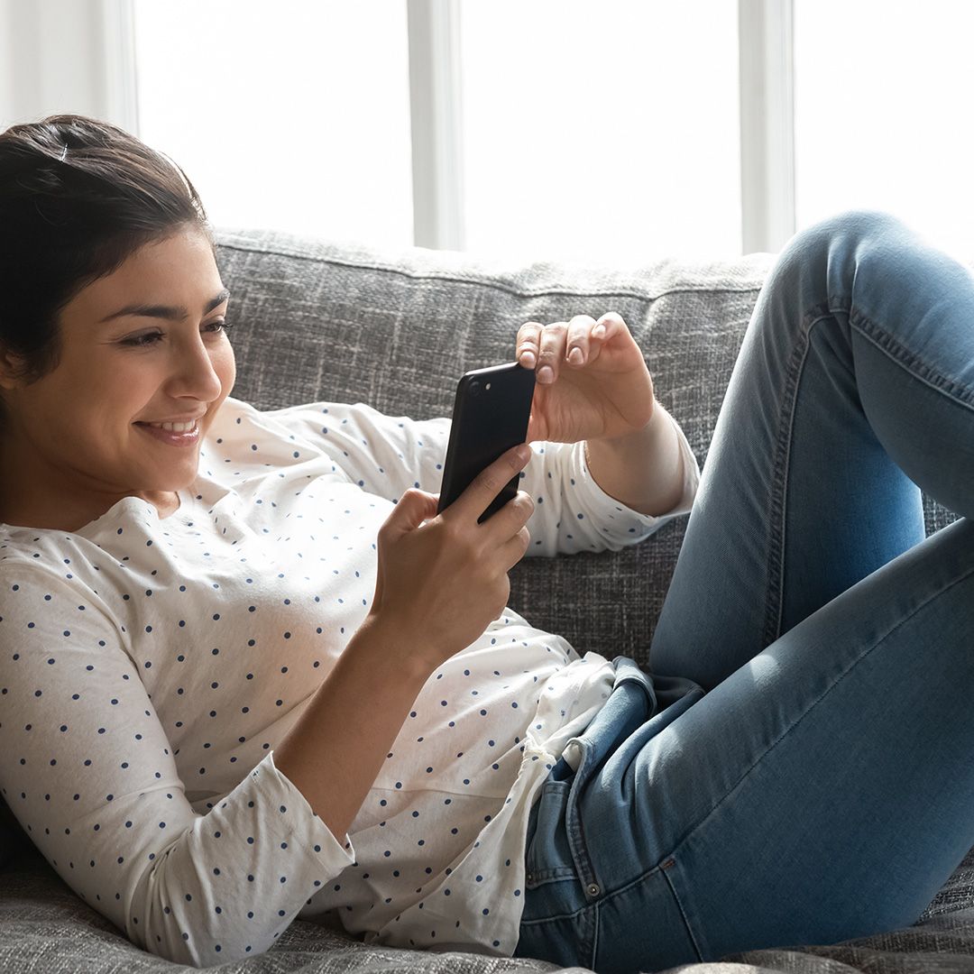 Indian woman on couch smiling at smart phone