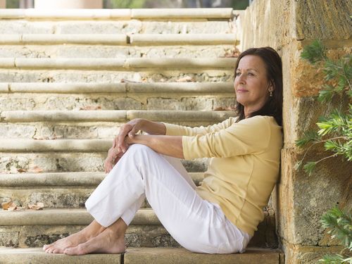 Women sitting alone on concrete stairs in an urban setting without shoes on. 