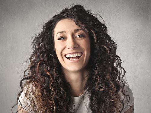 Portrait of a woman with a big smile against a light grey/white background.