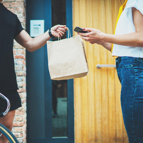 Delivery man handing delivery bag to woman holding a mobile phone