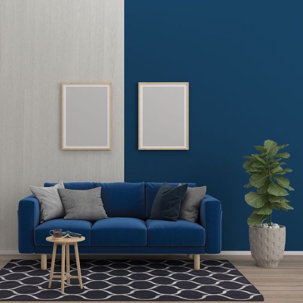 Room with one gray wall and one blue wall with two gray paintings and a blue couch. 