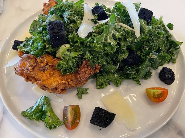 Fried chicken kale caesar salad staged on dinner plates.