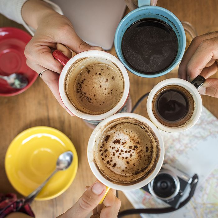 An image of four people touching their coffee cups together.