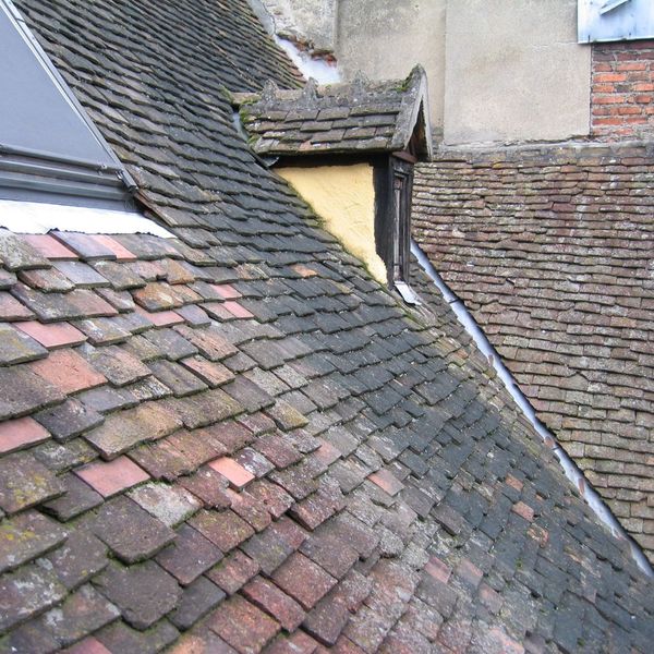 lose-up of an old, moss-covered tile roof with some broken and discolored tiles, indicating age and wear. lose-up of an old, moss-covered tile roof with some broken and discolored tiles, indicating age and wear.