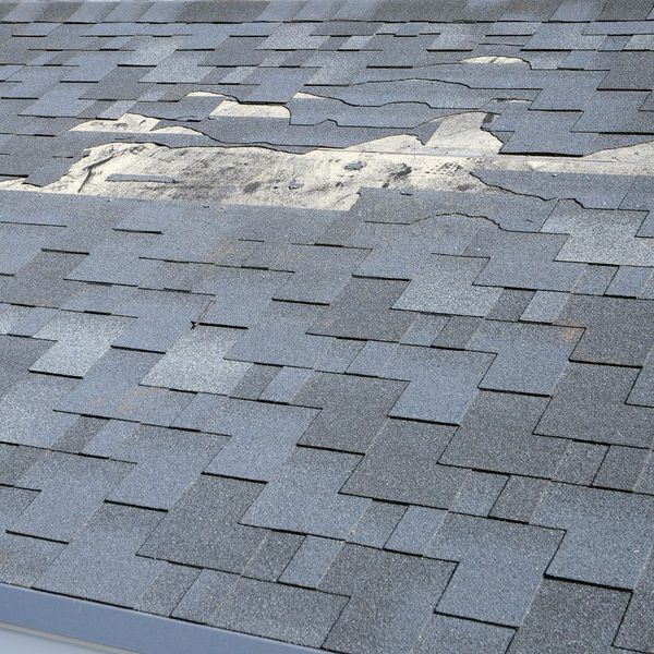 Close-up of a damaged asphalt shingle roof with several missing and torn shingles revealing the underlayment. Close-up of a damaged asphalt shingle roof with several missing and torn shingles revealing the underlayment.