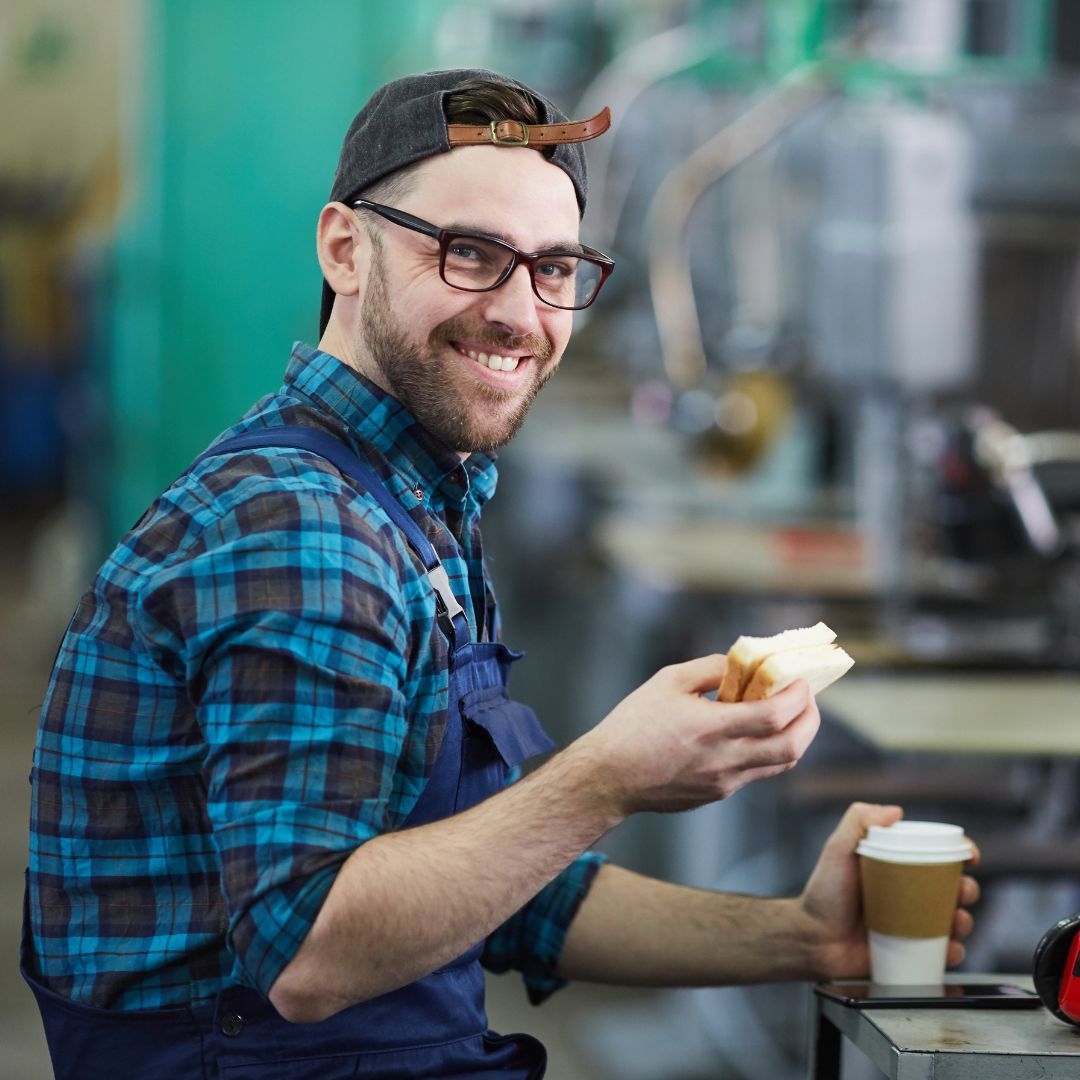 A manufacturing worker eating a sandwich and drinking coffee on a break