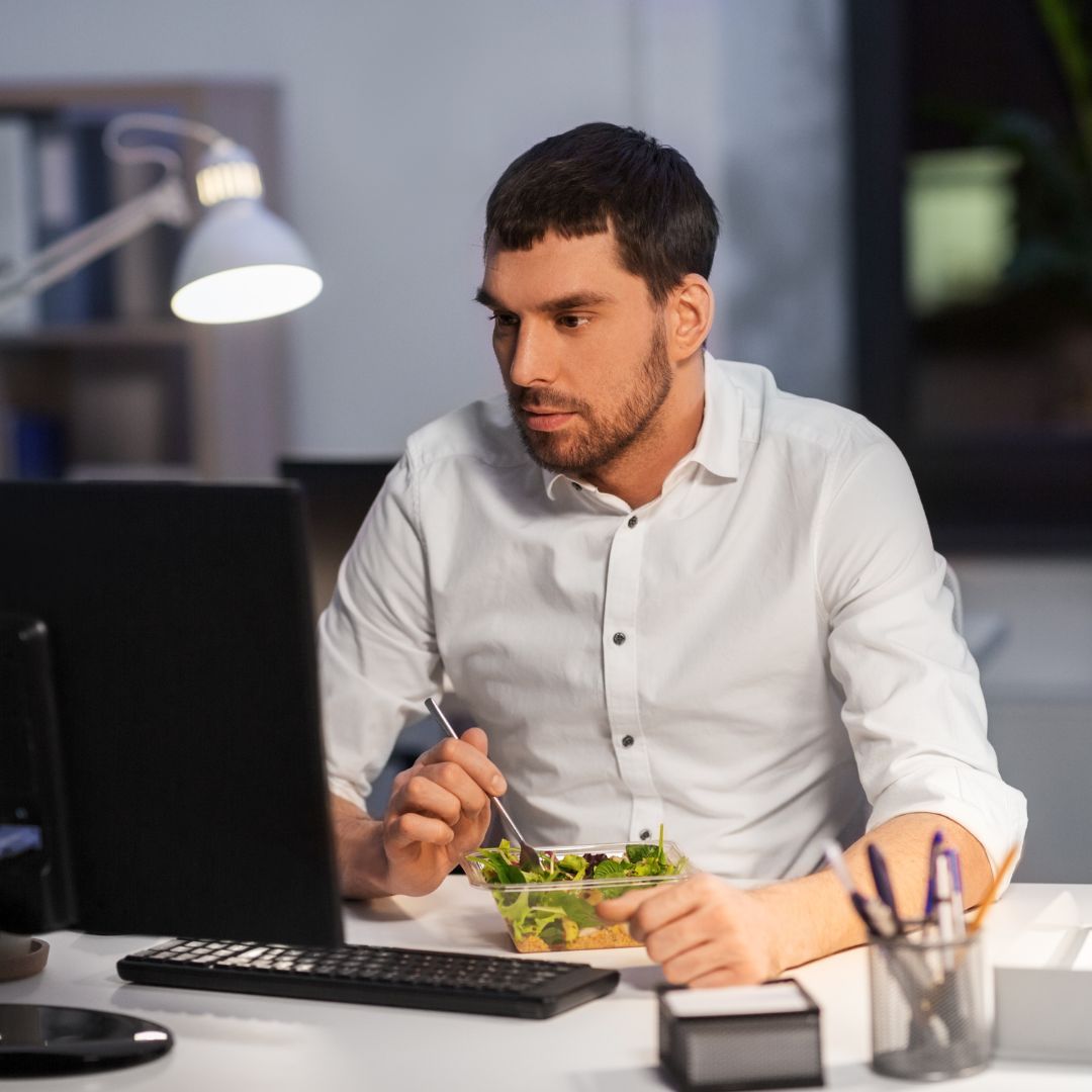 man eating salad at computer