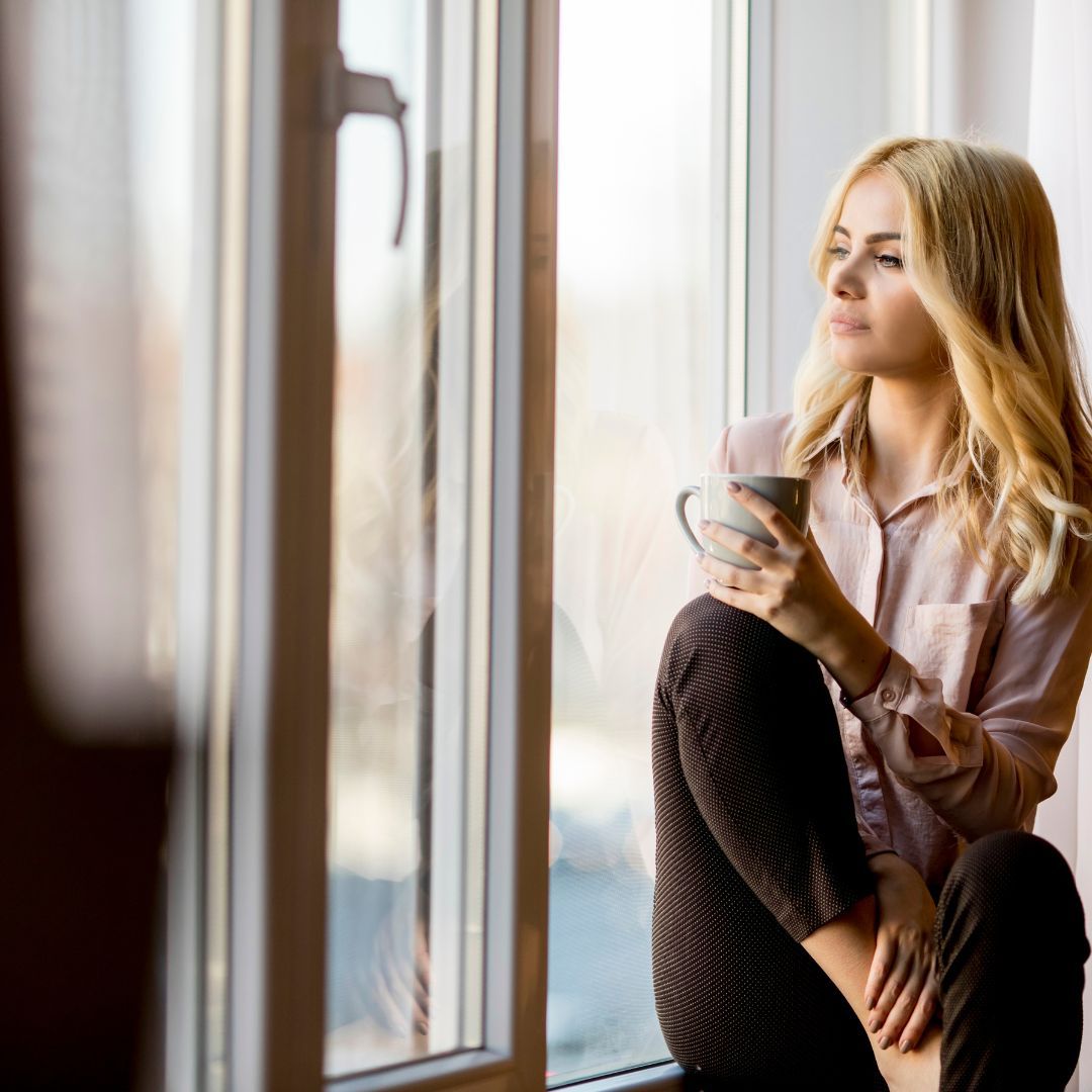 woman looking out window with coffee cup