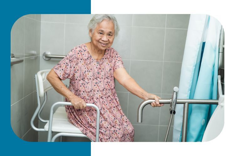 Elderly person clothed and sitting in a shower chair and holding a grab bar